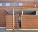 A corrugated corten steel façade wraps the entire facade interrupted by ribbons of black fiber-cement siding and windows. The protected residential entry porch provides secure storage for wet and dirty gear.