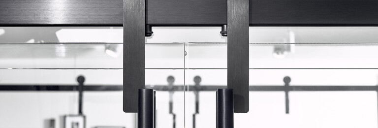 Close Up of Oden Glass Mount Trolleys in Black Stainless