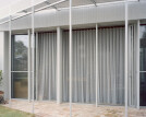 Sheer, dove grey curtains skirt the interior glazing on the ground floor, softening the transition between inside and outside.