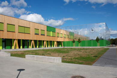 The cladding on the school building is a combination of wood, green panels and reflective façades.