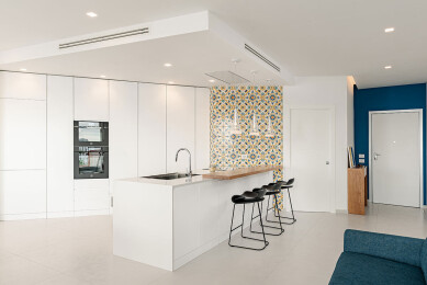 Open-plan entry with bespoke kitchen with peninsula in total white and an accent of color with the blue wall and majolica tiles