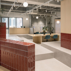 Glazed crimson tiles meet wood and exposed concrete in this vibrant workspace designed by Yatofu