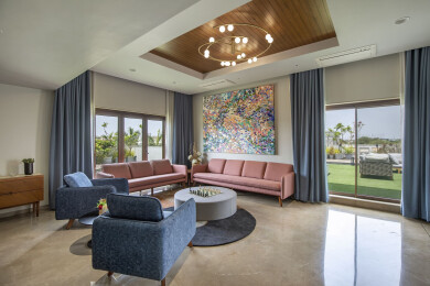 The beautiful blue and blush pink couches and a spiral chandelier add charm to this area. With large works of art displayed beside concrete walls, the spaces evoke an art gallery-like aesthetic.