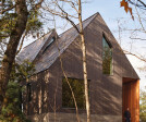 Natural materials were chosen to complement the rustic context. Greyed wood siding contrasts the natural cedar soffits and screen framing the entrance, sitting atop the raw, board-formed concrete base.